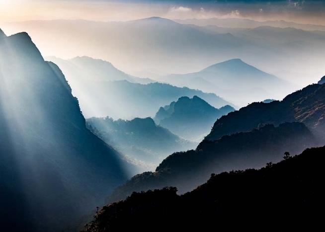 – Photographie de montagnes brumeuses traversées par le soleil.
