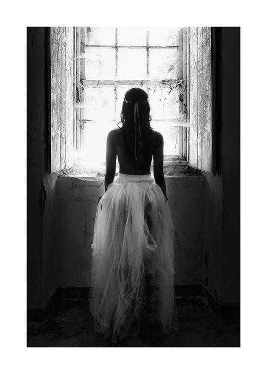 Photographie en noir et blanc d’une femme en robe de tulle debout devant une fenêtre