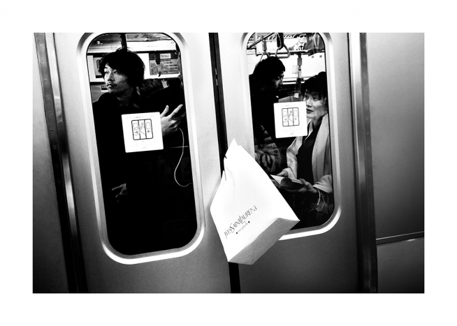 Photographie en noir et blanc d’un sac de courses coincé entre les portes d’un train