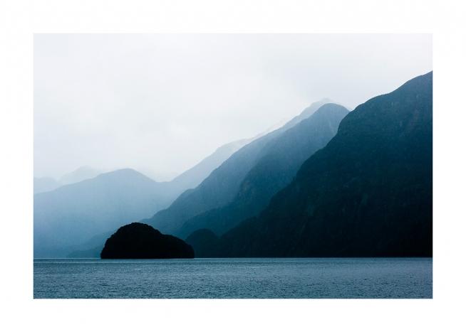  - Photographie de la mer devant des montagnes bleues avec des couches de brouillard derrière