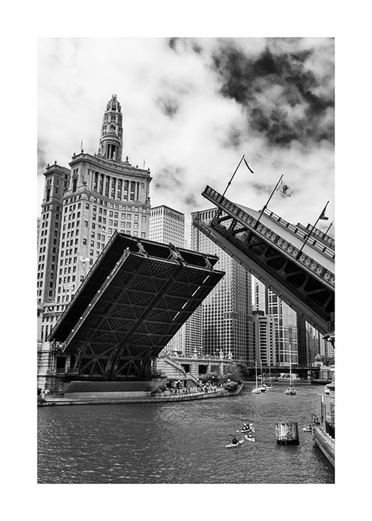  - Photographie en noir et blanc du pont de Chicago en pleine ouverture. Nous pouvons apercevoir des bâteaux sur le fleuve et des bâtiments en arrière-plan