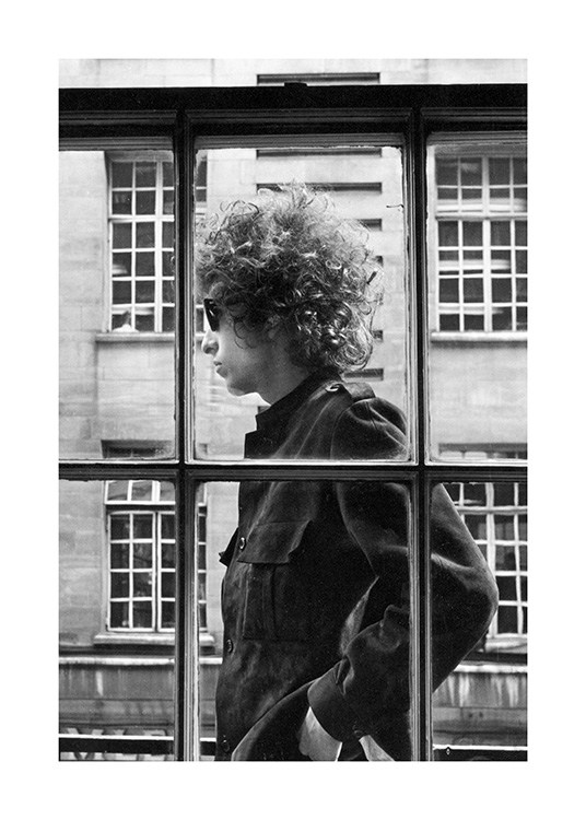  - Photographie en noir et blanc de Bob Dylan, il se tient dehors derrière une fenêtre