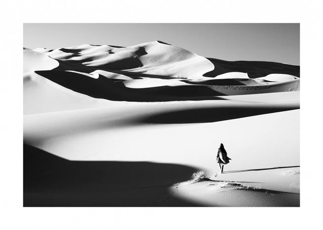  – Photographie en noir et blanc d’un désert, avec une femme marchant dans les dunes de sable