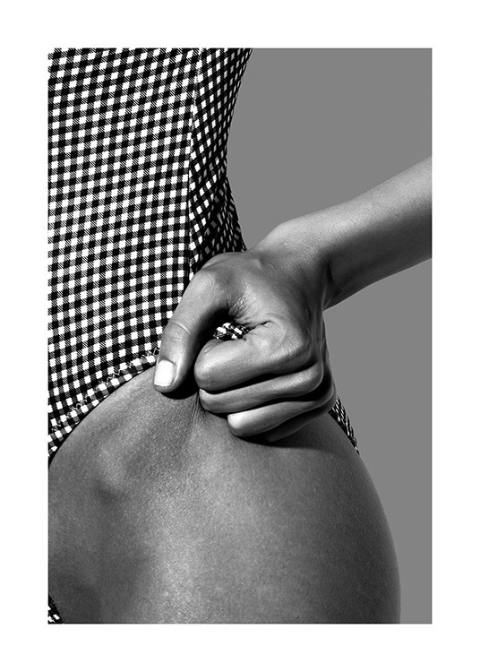  – Photographie en noir et blanc d’une femme en maillot de bain à carreaux, tenant le bord du maillot sur sa hanche