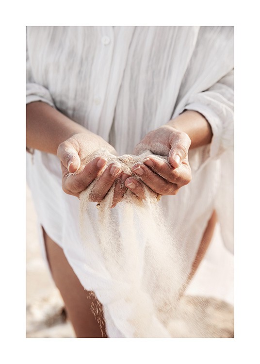  – Photographie d’une femme tenant du sable dans ses mains, avec sa chemise blanche en lin à l’arrière-plan