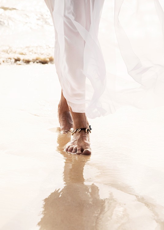  – Photographie en gros plan des pieds d’une femme, elle porte un bracelet de cheville et marche sur le sable