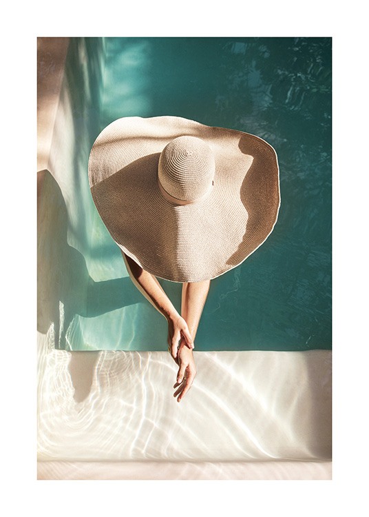  – Photographie d’une femme portant un chapeau de soleil, debout dans une piscine avec les bras tendus devant elle