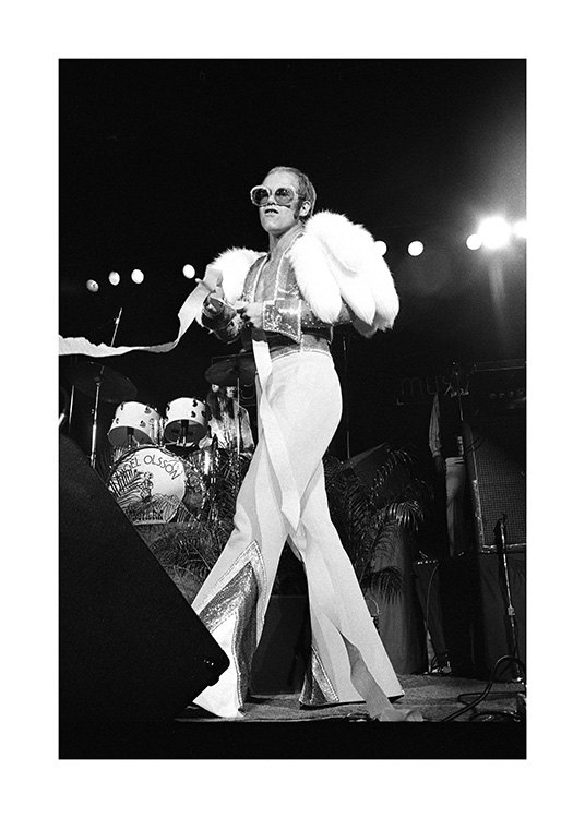  – Photographie en noir et blanc du chanteur Elton John, portant une combinaison blanche et des lunettes de soleil sur scène