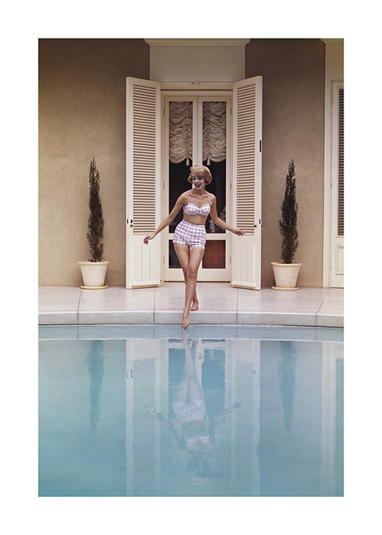  – Photographie d’une femme trempant son pied dans une piscine, portant un bikini de style vintage rose et blanc