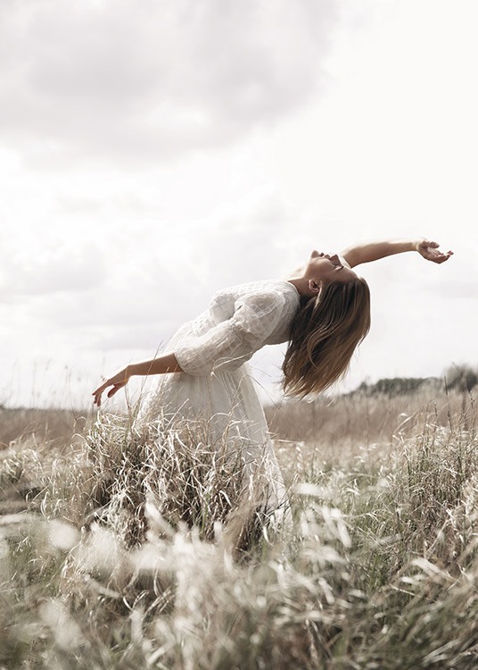  – Photographie d’une femme posant dans un champ avec l’herbe, portant une robe blanche