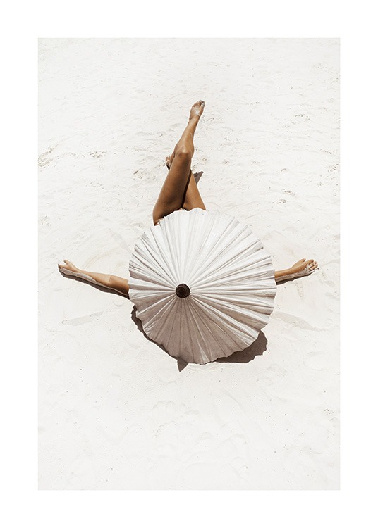  – Photographie d’une femme dissimulée par un parasol beige, couchée sur du sable blanc avec les jambes croisées