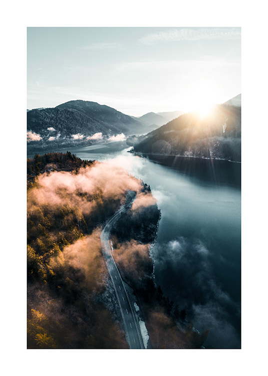  – Photographie d’un paysage avec une route entre une forêt et un lac, avec des montagnes et le soleil à l’arrière-plan