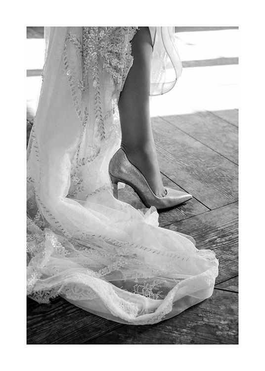  – Photographie en noir et blanc de l’extrémité d’une robe blanche avec des broderies et une chaussure à talon haut