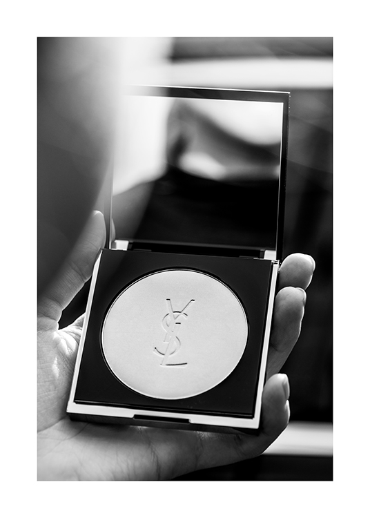  – Photographie en noir et blanc d’une personne tenant un poudrier YSL avec un miroir