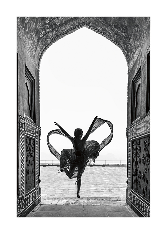  – Photographie en noir et blanc d’une femme en train de danser sur une jambe dans une robe fluide, encadrée par une arche