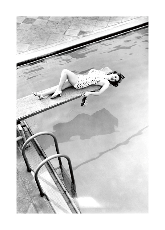  – Photographie en noir et blanc d’une femme allongée sur un plongeoir avec une piscine dessous
