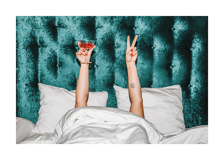  – Femme tenant une boisson orange dans un lit avec une tête de lit en velours turquoise