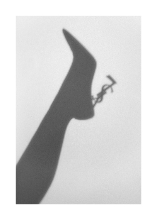  – Photographie de l’ombre sur un mur gris clair d’une jambe et d’un escarpin avec le logo YSL en guise de talon