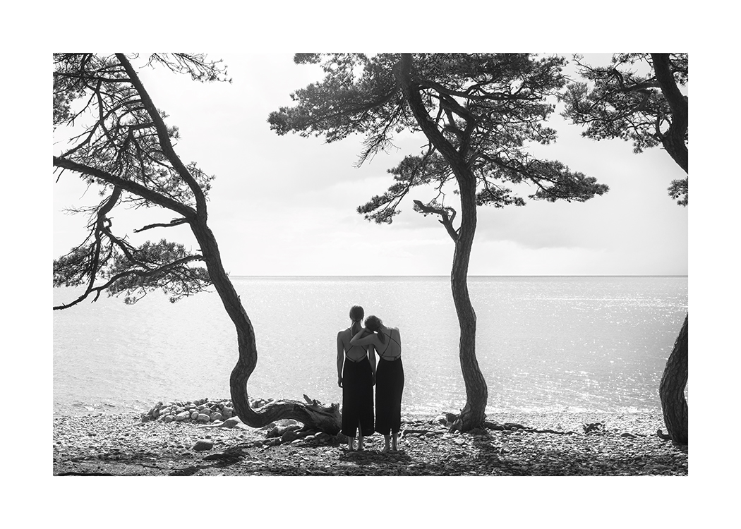  – Photographie en noir et blanc d’un couple de femmes contemplant l’eau depuis une plage avec des arbres