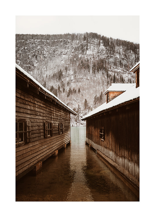  – Photographie de deux hangars à bateaux devant une montagne avec une forêt enneigée