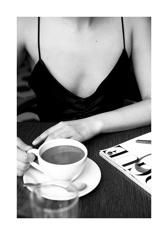  – Photographie en noir et blanc d’une femme assise dans un café avec une tasse de café sur la table