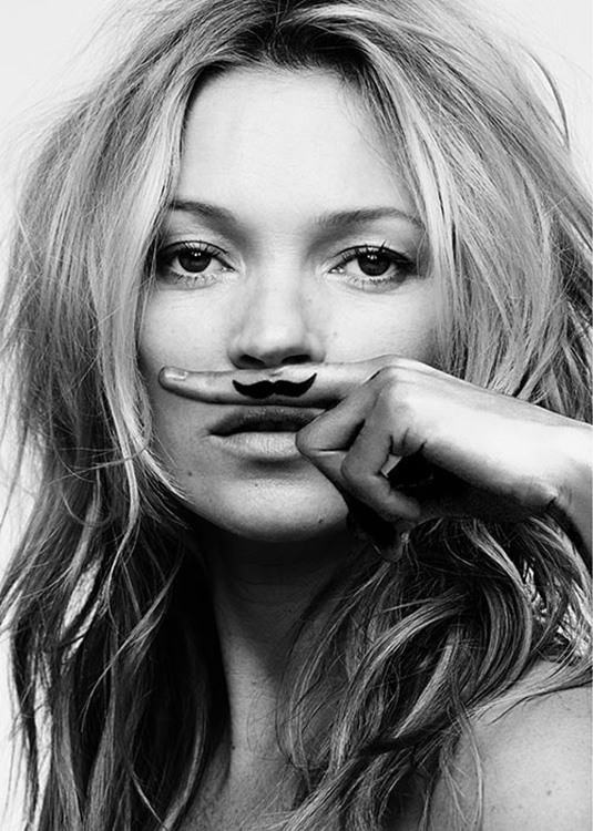  – Photographie en noir et blanc de Kate Moss avec un doigt au-dessus de la bouche avec une moustache sur le doigt